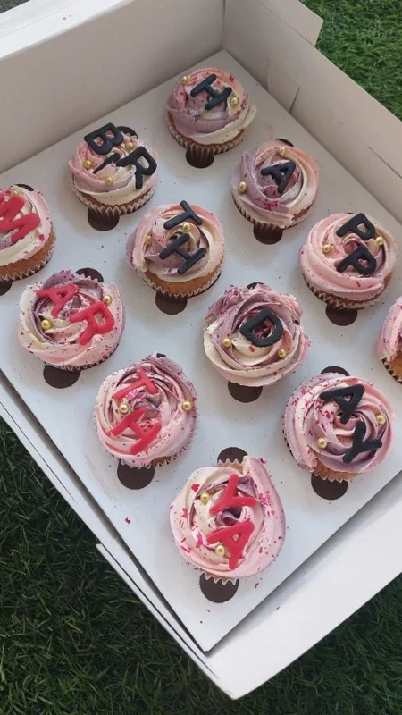 Box of pink and mauve cupcakes spelling Happy Birthday